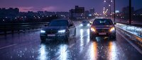 Cars driving on wet highway at night with headlights illuminating rain drops and city skyline in background during purple twilight hour.