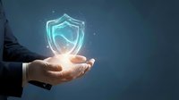 Businessman holding glowing shield hologram in cupped hands against blue background, representing digital security, data protection, and cybersecurity solutions.