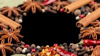 Aromatic spices frame creating copy space with cinnamon sticks, star anise, peppercorns and chili peppers for culinary design and food photography.