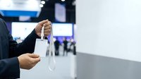 Businessman holding medical face mask at conference or trade show event with blurred crowd background.