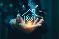 Businessman hand holding glowing house icon with target and business symbols on dark background for real estate investment marketing concept.