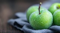 Fresh green apple with water drops on dark background, selective focus. Natural organic fruit macro photography for healthy eating concept.
