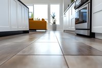 Low angle view of modern kitchen floor with white cabinets and orange sofa in background, showcasing clean minimalist interior design and natural lighting.