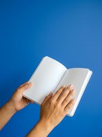 Open notebook with blank pages held by hands against blue background, suitable for education, writing, journaling, and learning concepts.