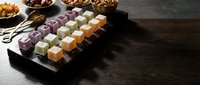 Colorful sushi rolls arranged on black slate board with chopsticks and side dishes on dark wooden table for Japanese cuisine dining experience.