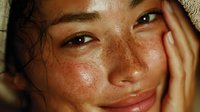 Young Asian woman with freckles touching face in natural light showing healthy glowing skin for skincare and beauty wellness lifestyle concepts.