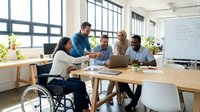 Diverse business team collaborating in modern office meeting room with wheelchair accessibility and natural lighting for corporate teamwork.