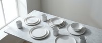 Minimalist white ceramic dinnerware set with plates bowls and cups arranged on marble table in bright modern kitchen interior for dining decor.