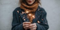 Young woman in cozy sweater holding sparkler creating magical light effects during winter celebration or holiday season.