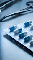 Blue and white capsule pills in blister pack with stethoscope on medical desk for healthcare and pharmaceutical treatment concepts.