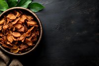 Crispy sweet potato chips in wooden bowl with fresh green leaves on dark stone background, healthy homemade vegetable snack for natural eating.