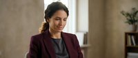 Professional businesswoman in burgundy blazer smiling confidently in modern office environment for corporate presentations and leadership content.