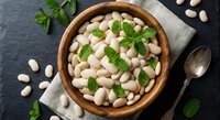 White cannellini beans in wooden bowl with fresh parsley on dark slate background. Healthy protein-rich legumes for cooking and meal preparation.