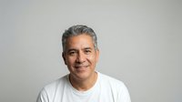 Middle-aged Hispanic man with gray hair smiling warmly in white t-shirt against neutral background for lifestyle and portrait photography projects.