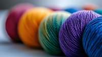 Colorful yarn balls arranged in rainbow order with selective focus on purple and blue threads, showing detailed texture of knitting materials.