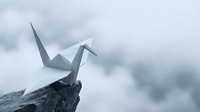 White origami paper crane perched on rocky cliff edge against dramatic cloudy sky background symbolizing hope freedom and peaceful meditation.