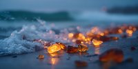 Golden amber pieces scattered on wet beach sand with ocean waves and warm glowing lights creating magical coastal atmosphere during twilight hour.