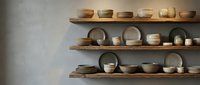 Handcrafted ceramic bowls and pottery displayed on wooden shelves against neutral wall, showcasing artisan craftsmanship and minimalist home decor style.