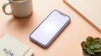 Modern smartphone with blank purple screen on minimalist desk workspace with coffee mug, notebook and succulent plant for mockup presentations.
