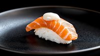 Fresh salmon nigiri sushi with creamy sauce on black ceramic plate against dark background, traditional Japanese cuisine served in restaurant setting.