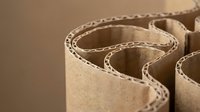Rolled corrugated cardboard sheets with visible fluted structure for packaging and shipping applications in manufacturing industry.