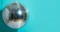 Shiny silver disco ball with mirror tiles reflecting light against vibrant turquoise background for party and nightlife entertainment events.