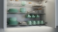 Organized kitchen cabinet with mint green dishes, mugs, and bowls on wire shelves, showcasing modern storage solutions for home interiors.