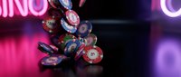 Colorful casino poker chips falling and scattered on dark surface with bright neon lights creating vibrant pink and purple atmosphere for gambling entertainment.