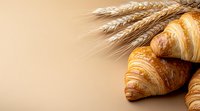 Fresh baked croissants with golden wheat ears on beige background, copy space for bakery menu, food photography for restaurant promotion.