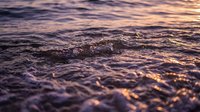 Gentle ocean waves at golden hour with warm sunlight reflecting on water surface creating peaceful seascape atmosphere for relaxation and meditation backgrounds.
