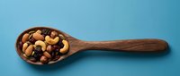 Wooden spoon filled with mixed nuts and dried fruits on blue background for healthy snacking and cooking concepts.