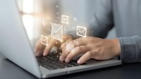 Person typing on laptop with glowing email icons floating above keyboard, representing digital communication and message sending in business environment.