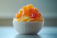 Creamy vanilla soft serve ice cream topped with colorful fruit gummy candies in white bowl on clean surface for dessert and confectionery concepts.