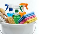 Cleaning supplies in white bucket with colorful microfiber cloths, spray bottles, brushes and detergents isolated on white background for housework.