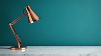 Copper desk lamp with adjustable arm positioned against teal wall and marble surface, suitable for interior design, home decor, and workspace styling projects.