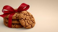 Homemade oatmeal cookies tied with elegant red ribbon bow on beige background, festive holiday treat or gift concept for special occasions.
