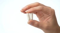 Hand holding white medical pills or capsules between fingers on clean white background for healthcare and pharmaceutical concepts.