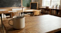 Coffee mug on wooden desk in empty classroom with chalkboard and chairs, back to school concept for education and learning environments.