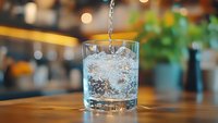 Fresh water pouring into glass with ice cubes on wooden bar counter in restaurant setting with bokeh lights background for beverage service.