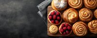 Fresh baked sweet cinnamon rolls and ripe red raspberries served on wooden cutting board against dark background, top view with copy space.