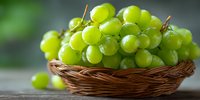 Fresh green grapes in wicker basket on wooden table with natural lighting for healthy eating and organic fruit concepts.