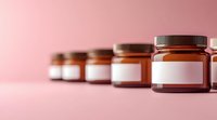 Brown glass cosmetic jars with blank labels arranged in row on pink background, selective focus on front jar, minimalist product mockup for skincare packaging.