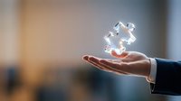 Businessman hand holding glowing puzzle pieces floating above palm representing problem solving and strategic thinking in corporate environment.