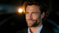 Caucasian male model with beard wearing business suit smiling confidently at sunset with warm backlight creating dramatic portrait lighting effect for professional headshot.