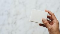 Close-up of hand holding blank white box against marble background, suitable for product packaging mockups and branding presentations.