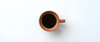 Orange ceramic coffee cup filled with black coffee viewed from above on white background for morning beverage and cafe design projects.