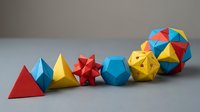 Colorful geometric paper shapes arranged in a row including pyramids, stars, and polyhedrons in red, blue, and yellow for design and craft projects.