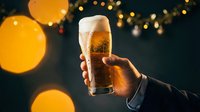 Hand holding a cold beer glass with foam head against dark background with golden bokeh lights, perfect for beverage advertising and celebration themes.