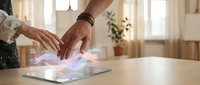 Hands interacting with futuristic holographic interface on tablet device in modern bright interior space for technology and innovation concepts.