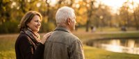 Happy mature couple enjoying romantic sunset walk in autumn park with golden light and peaceful lake reflecting warm evening glow creating intimate moment together.